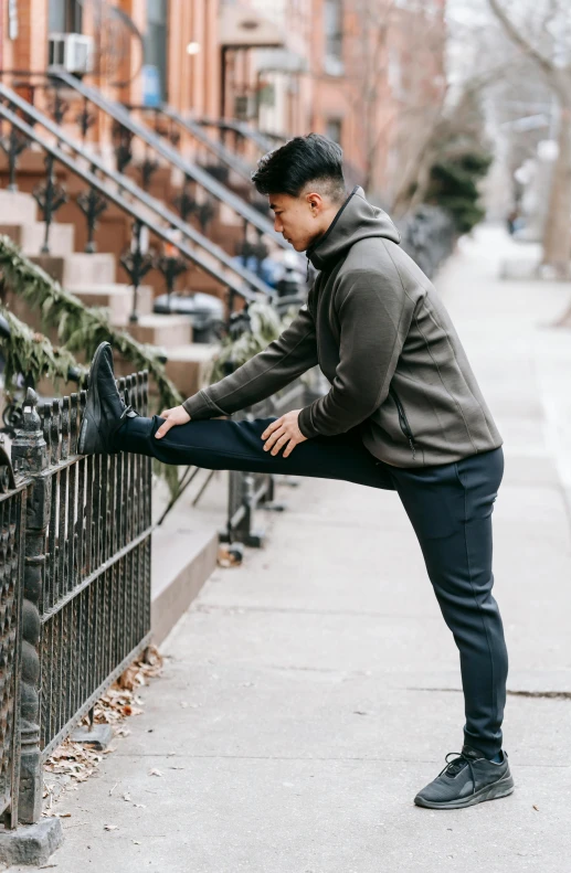 a man stretching his legs on a sidewalk, trending on unsplash, wearing track and field suit, bao pham, leaning on door, tights