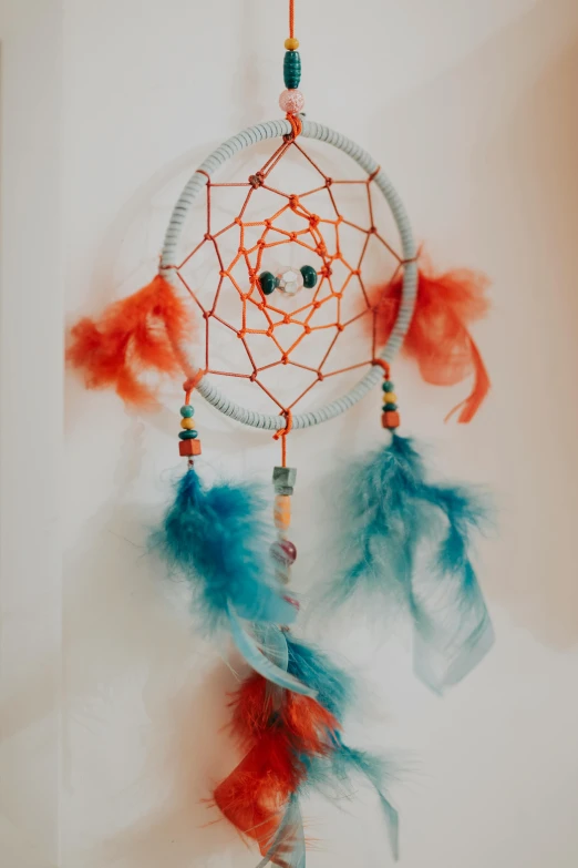 a colorful dream catcher hanging on a wall, by Annie Abernethie Pirie Quibell, orange and blue colors, twinkling and spiral nubela, crafts and souvenirs, red turquoise accents