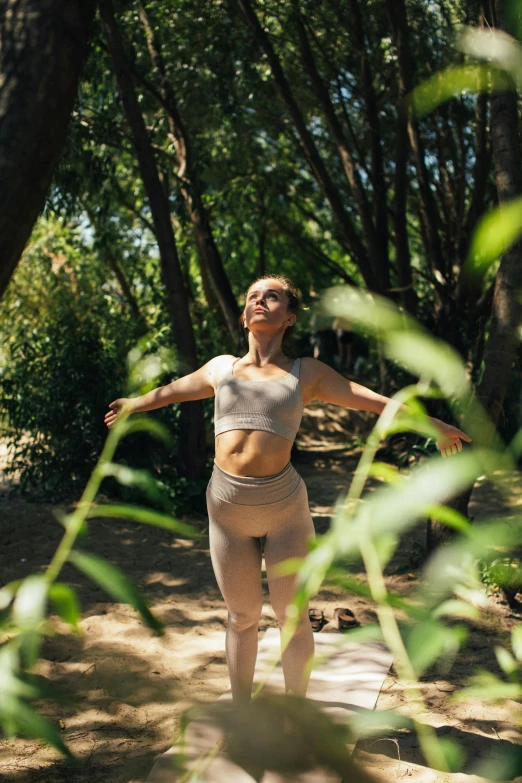 a woman that is standing in the dirt, lush surroundings, yoga pose, sun overhead, greenery