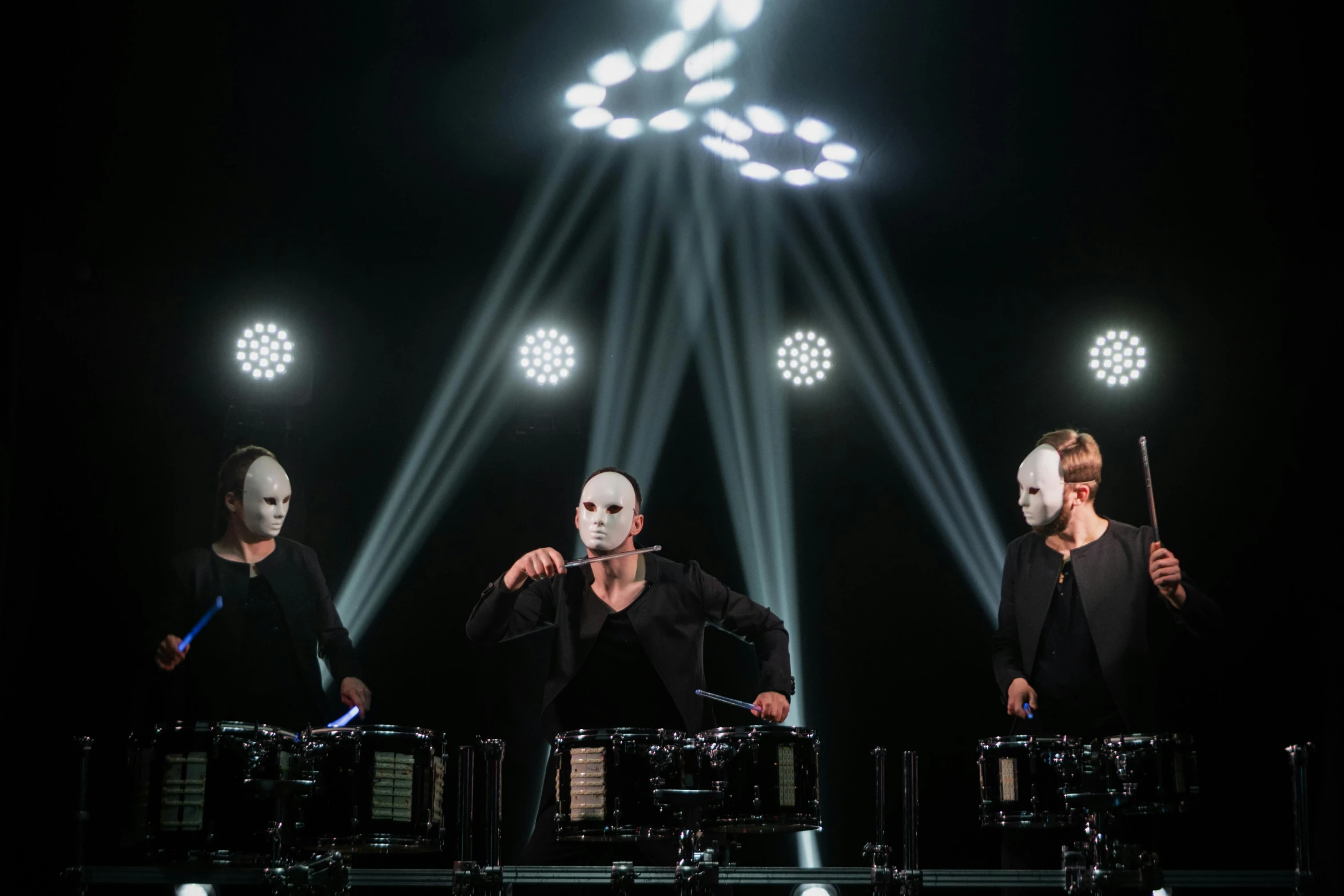 a group of men standing on top of a stage, a hologram, unsplash, antipodeans, elaborate lights. mask on face, drums, twins, set against a white background