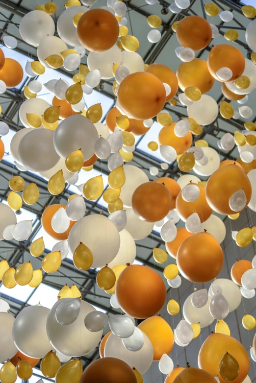 a bunch of balloons that are in the air, an abstract sculpture, inspired by Bruce Munro, unsplash, orange and white color scheme, large glass ceilings, taken in the late 2000s, golden dapple lighting