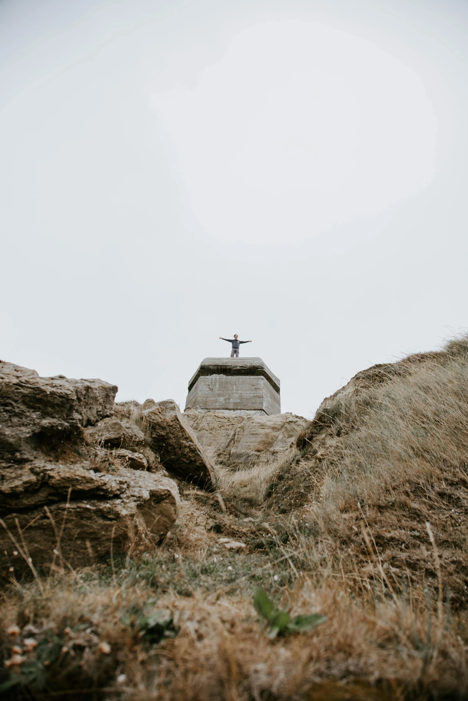 a cross on top of a large rock, a statue, unsplash, renaissance, normandy, distant full body view, heads, pov photo