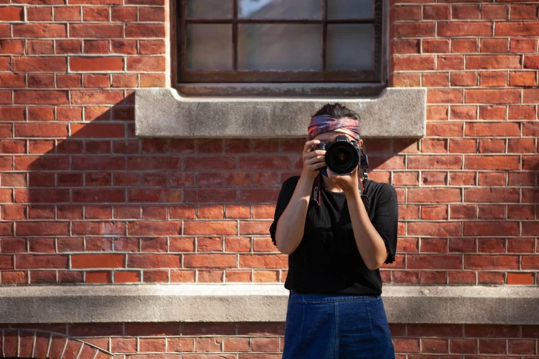 a woman taking a picture of herself in front of a brick building, a picture, inspired by Vivian Maier, unsplash, medium format, annie lebowitz, waist up portrait, shot on red camera