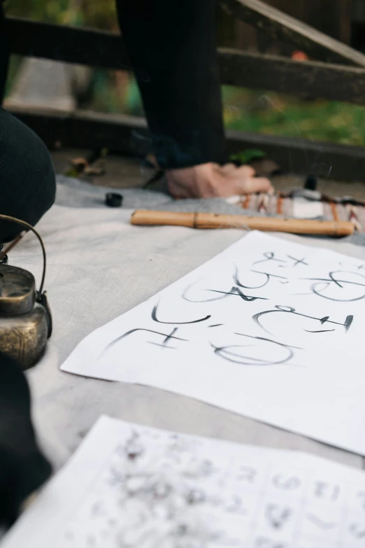 a person sitting on the ground writing on a piece of paper, inspired by Li Di, art & language, caligraphy, on a table, al fresco, ninja scrolls