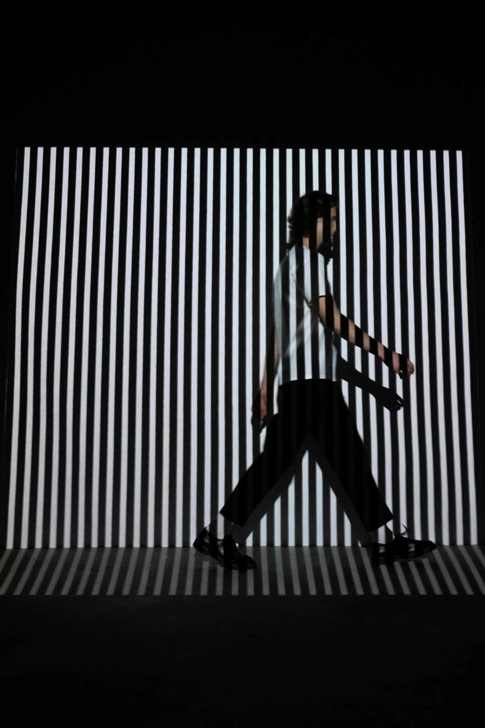 a man holding a tennis racquet on top of a tennis court, inspired by Ryoji Ikeda, video art, walks down dark hallway, black stripes, motion capture system, billboard image