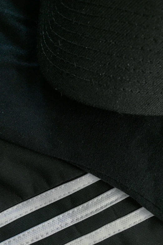 a black hat sitting on top of a pile of clothing, wearing adidas clothing, zoomed in, material study, sparse detail