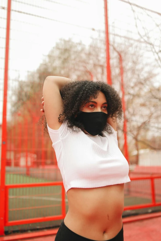 a woman standing on top of a tennis court holding a racquet, an album cover, trending on pexels, black bandana mask, wearing crop top, balaclava covering face, curly haired