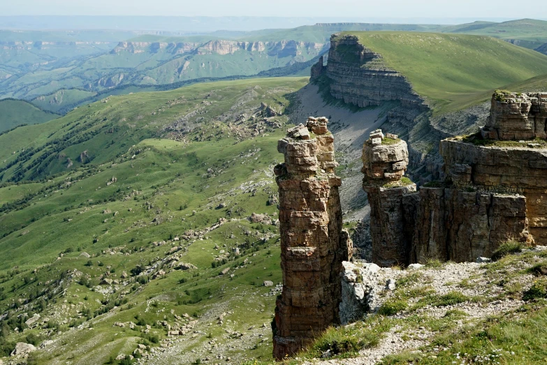 a couple of large rocks sitting on top of a lush green hillside, by Muggur, les nabis, spines and towers, rusty metal towers, overview, rock columns