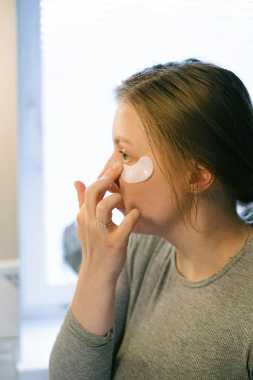 a woman putting eye cream on her face, by Julia Pishtar, reddit, wearing a patch over one eye, silicone skin, full body image, skimask