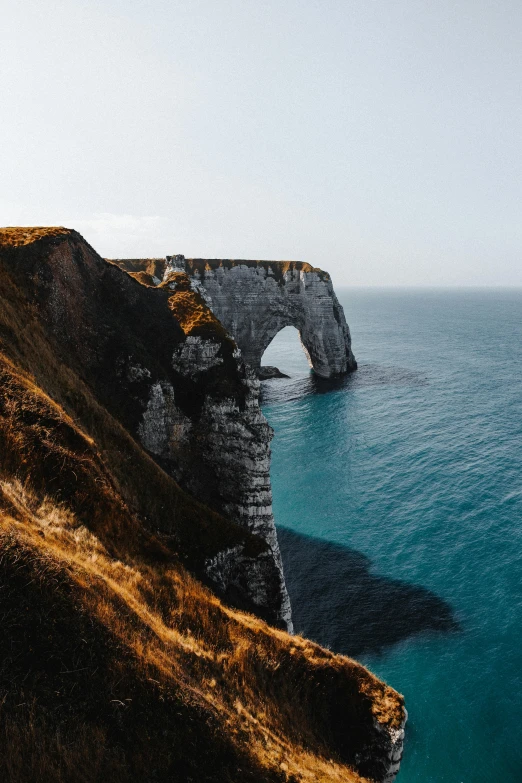 a man standing on top of a cliff next to the ocean, by Raphaël Collin, pexels contest winner, renaissance, massive arch, farming, over a chalk cliff, hd footage