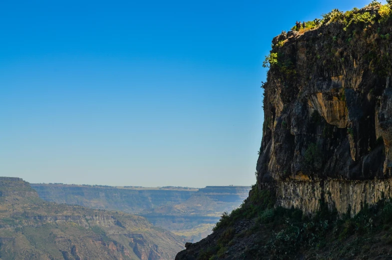 a group of people standing on top of a cliff, by Peter Churcher, pexels contest winner, hurufiyya, avatar image, blue sky, in between a gorge, panoramic