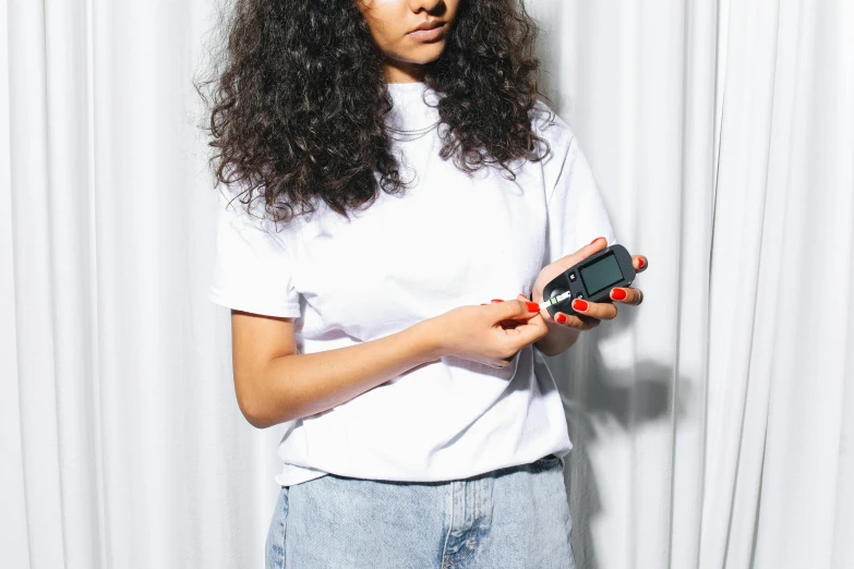 a woman standing in front of a white curtain holding a cell phone, trending on pexels, as fashion editorial 90s, white t-shirt with red sleeves, game and watch, curls on top