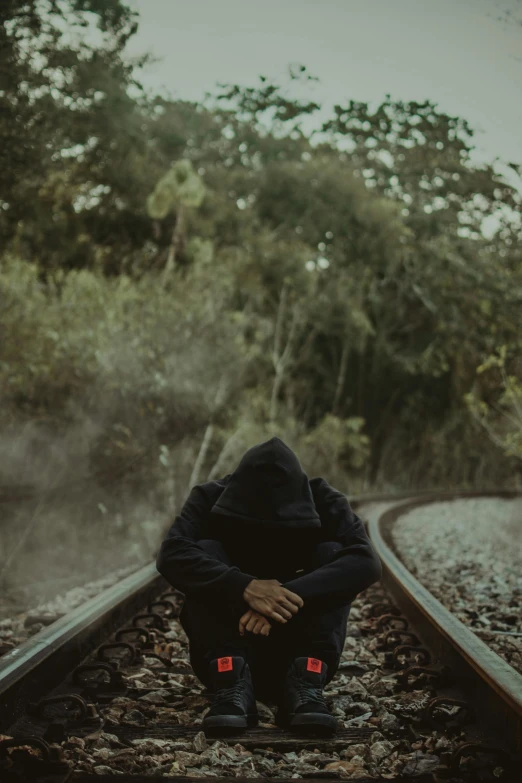 a person crouching down on a train track, pexels contest winner, portrait of mournful, hooded, slightly pixelated, low quality photo