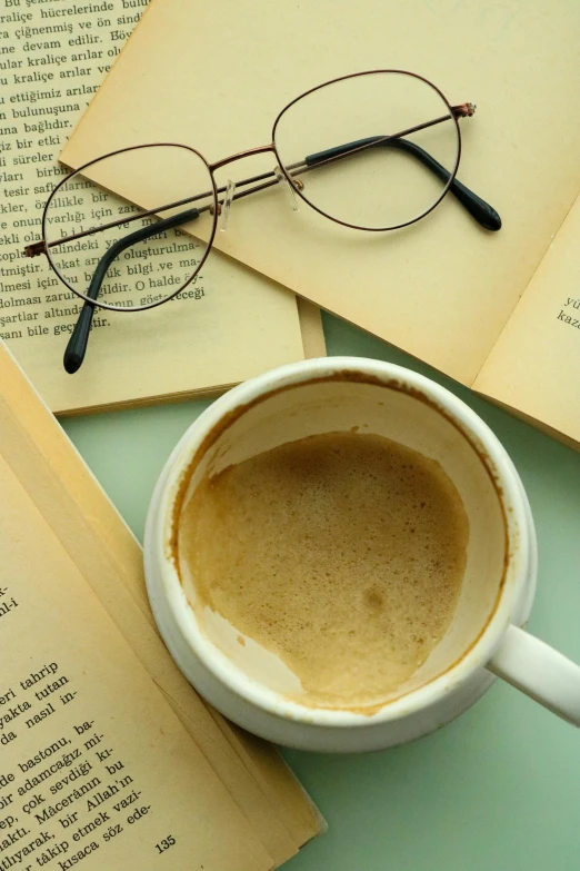 a cup of coffee next to an open book, thin round glasses, promo image, creamy, multiple stories