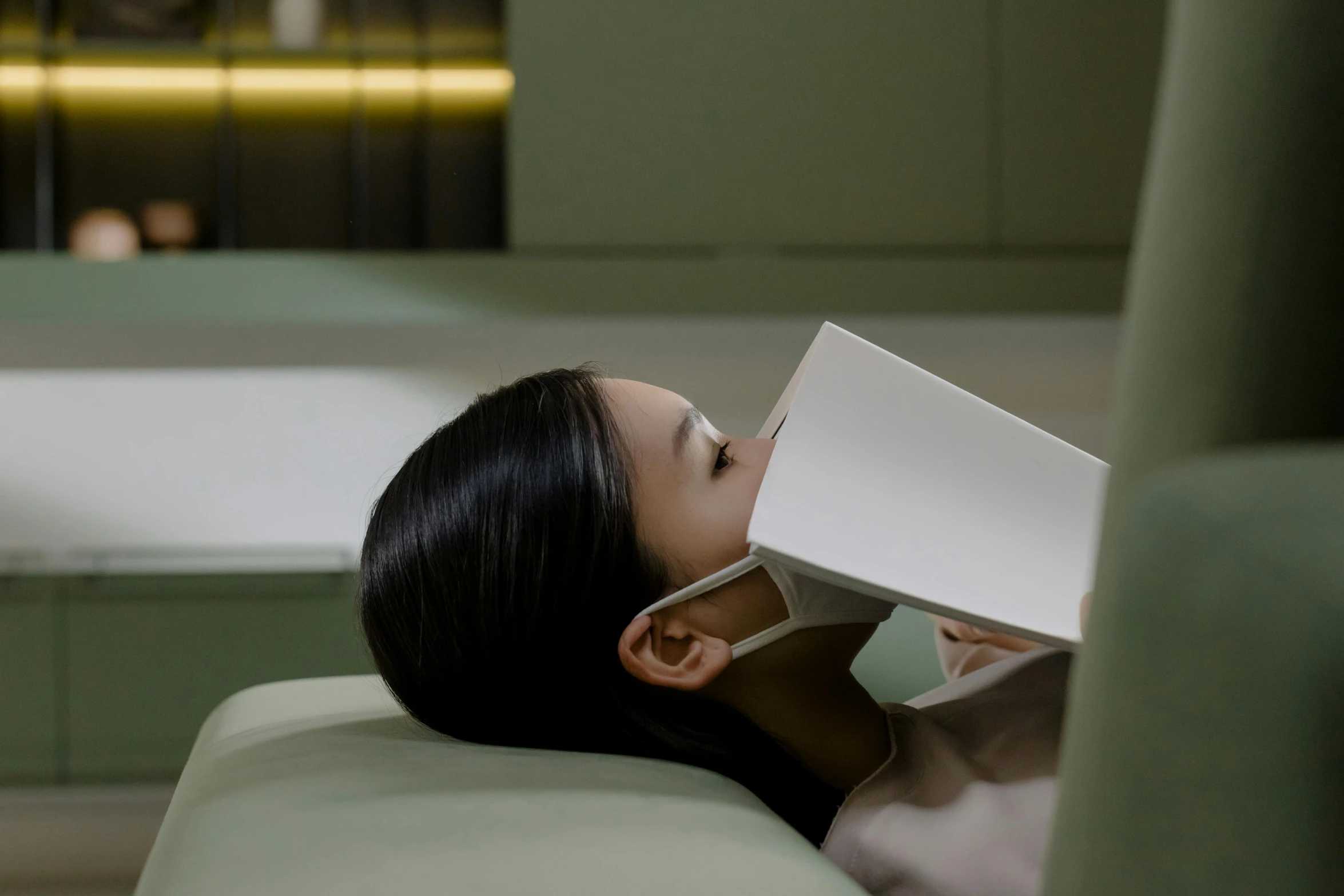 a woman laying on a couch reading a book, inspired by Fei Danxu, surgical mask covering mouth, square facial structure, dentist, ignant