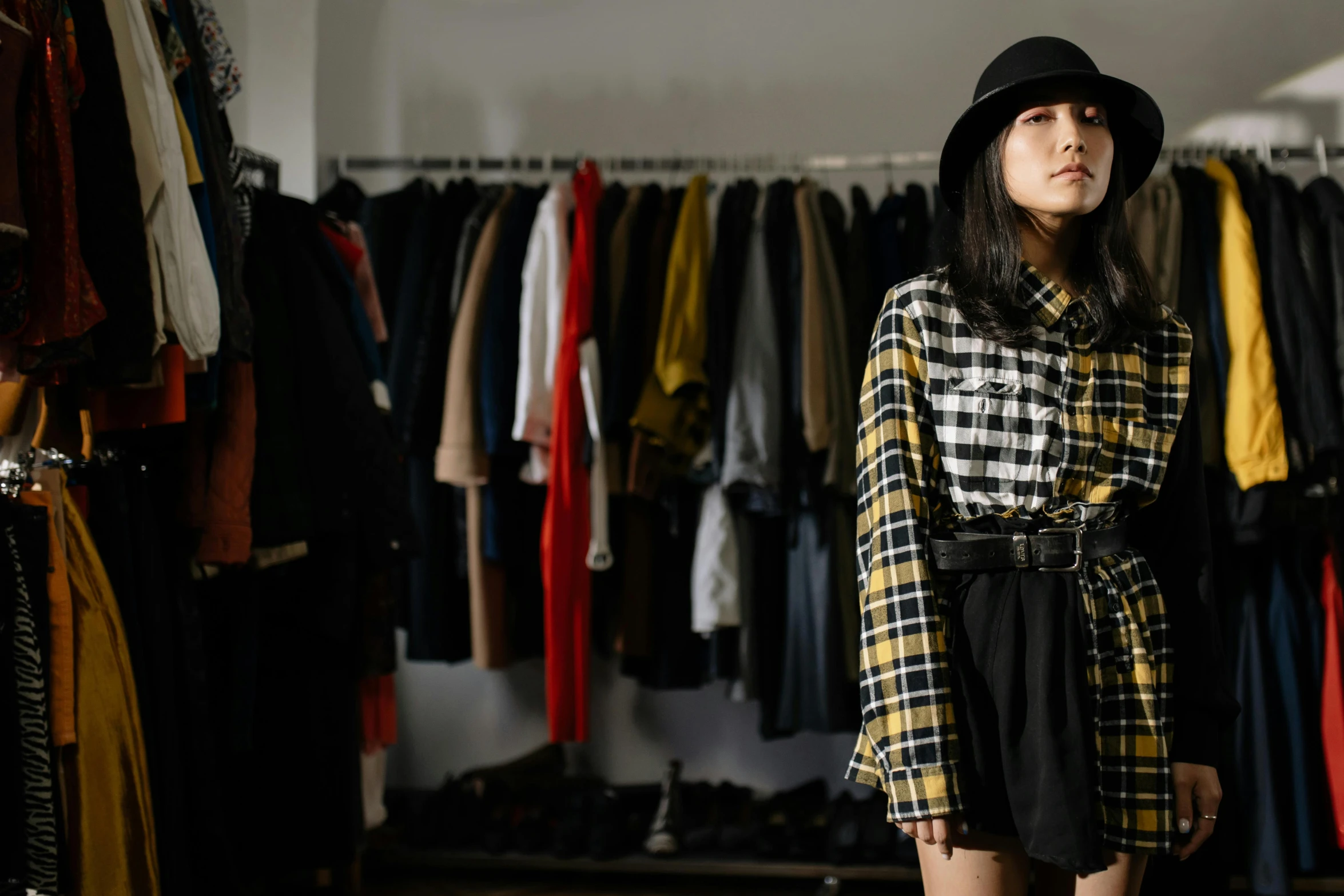 a woman standing in front of a rack of clothes, a portrait, trending on unsplash, realism, yellow and black, wearing plaid shirt, yohji yamamoto, a young asian woman