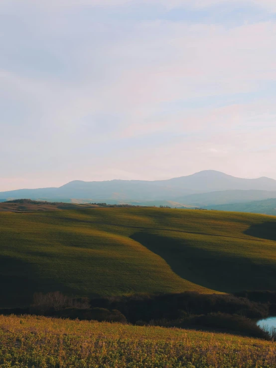 a body of water sitting on top of a lush green hillside, by Alexis Grimou, pexels contest winner, renaissance, on the vast wheat fields, with rolling hills, background image, overexposed photograph