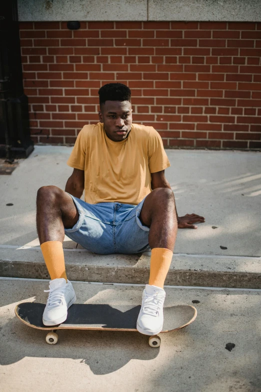 a man sitting on a step with a skateboard, by Washington Allston, trending on unsplash, realism, with brown skin, gold soccer shorts, yellow skin, wearing a shirt and a jean