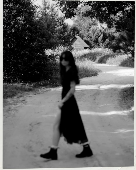 a black and white photo of a woman walking down a dirt road, a black and white photo, inspired by Nell Dorr, tumblr, gothic girl dressed in black, in style of valentin serov, dark shades, album art