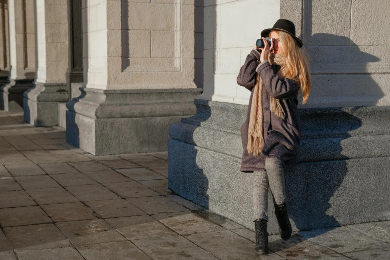 a woman taking a picture with her cell phone, inspired by Ruth Orkin, pexels contest winner, action shot girl in parka, madrid. extreme long shot, caracter with brown hat, dressed in a gray