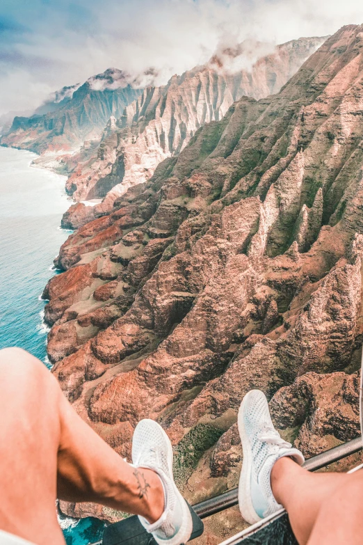 two people sitting on the edge of a cliff overlooking the ocean, white shorts and hiking boots, instagram story, airplane view, red sand beach