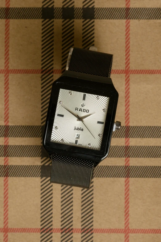 a close up of a watch on a plaid surface, an album cover, inspired by Joop Sanders, reddit, dada, black halo, detailed product photo, square, ( ivory black )