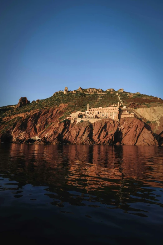 a small island in the middle of a body of water, cliffside town, red sand beach, peter marlow photography, palace of the chalice