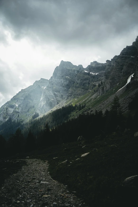 a view of a mountain range under a cloudy sky, dark pine trees, lauterbrunnen valley, light and dark, trending photo