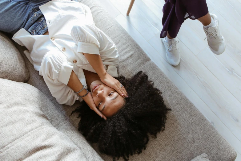 a woman laying on top of a couch next to a child, trending on pexels, happening, her hair is tied above her head, long afro hair, recovering from pain, on a white table