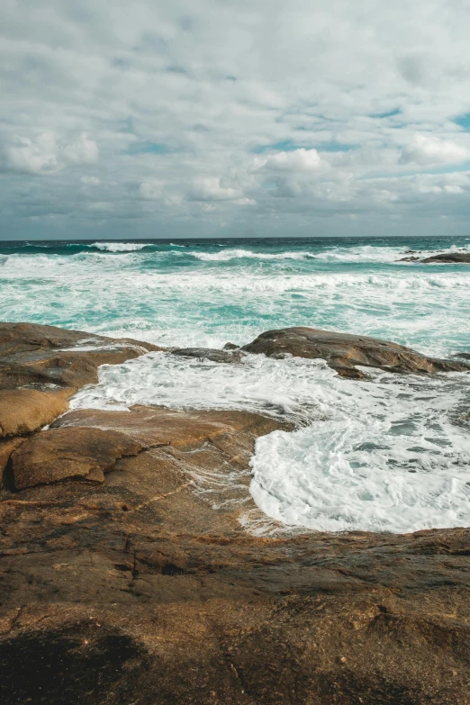 a man standing on top of a rock next to the ocean, by Elizabeth Durack, trending on unsplash, an eerie whirlpool, windy beach, clean 4 k, rippling muscles