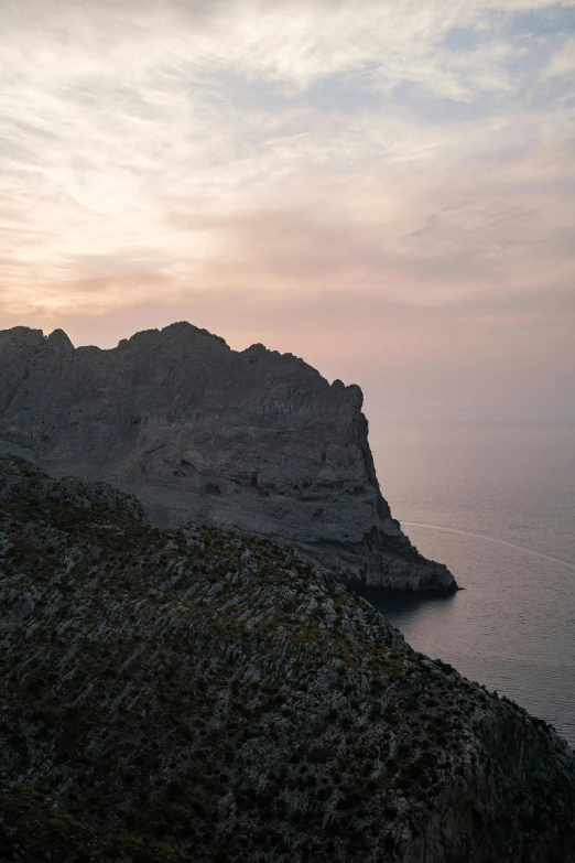 a man standing on top of a cliff next to the ocean, les nabis, sunset in the distance, calanque, muted colours, black domes and spires