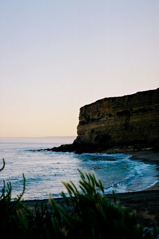 a man standing on top of a beach next to the ocean, cliff side at dusk, jerez, lush, bulli