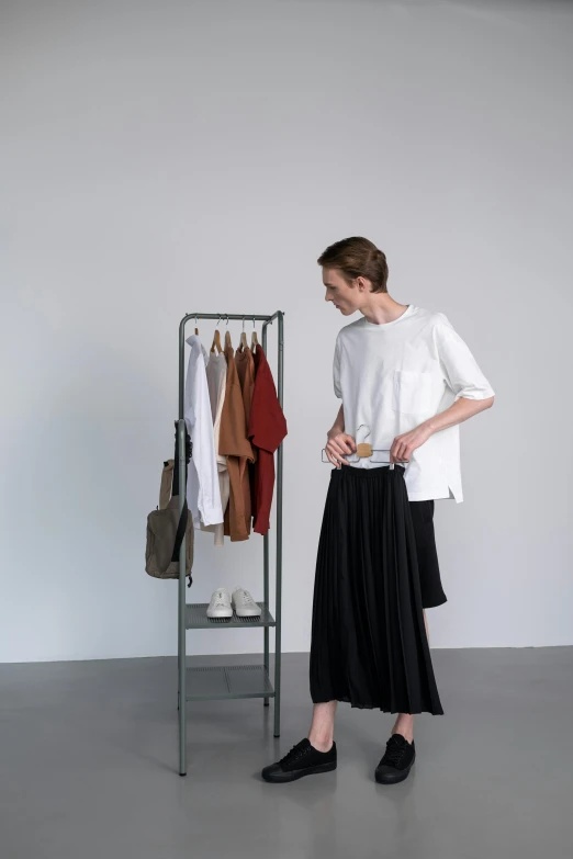 a woman standing in front of a rack of clothes, by Vadym Meller, happening, studio kyoto, product view, dressed in long fluent skirt, wearing pants and a t-shirt