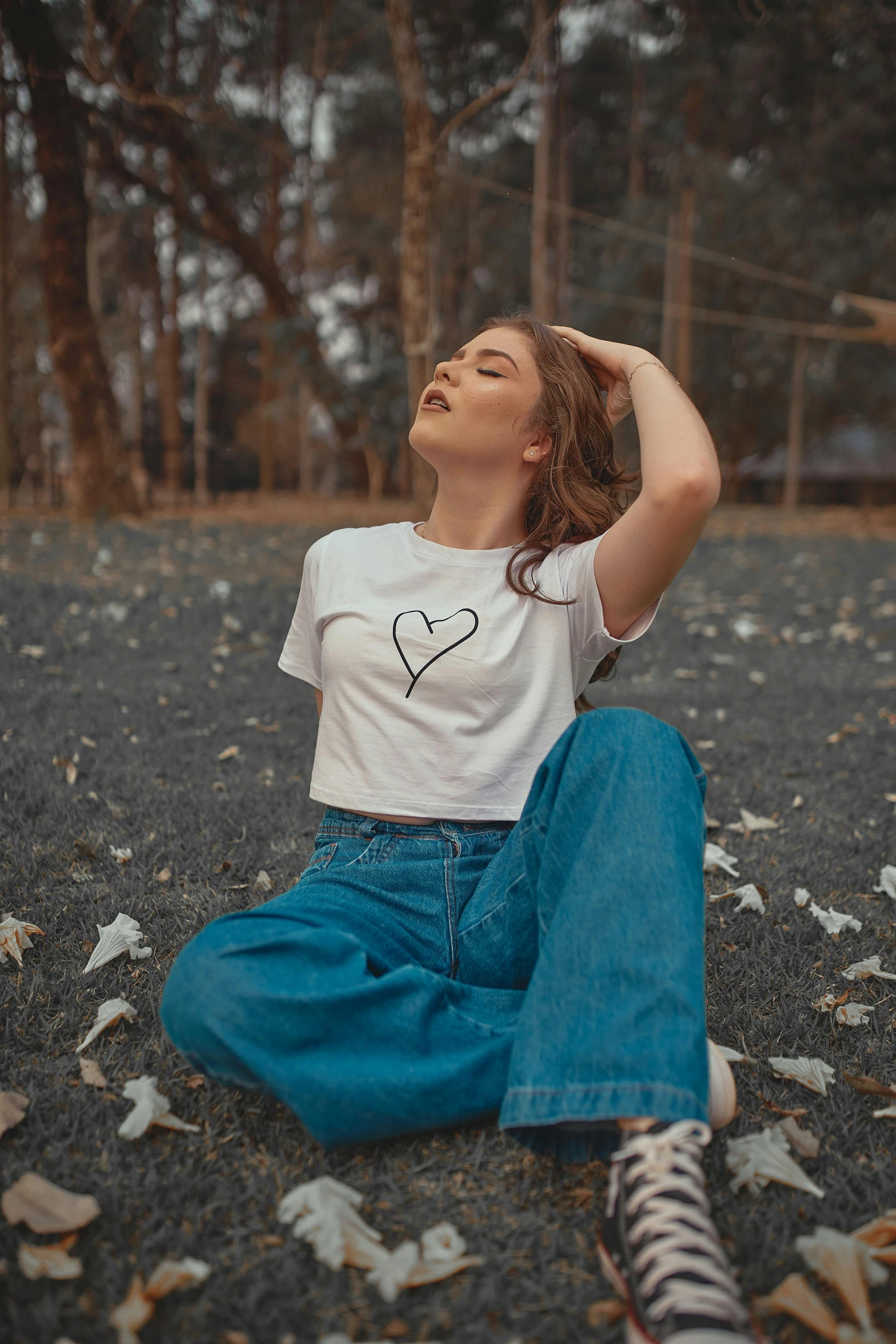 a woman sitting on the ground with her hands behind her head, trending on pexels, aestheticism, heart shaped face, graphic tees, federation clothing, jeans and t shirt