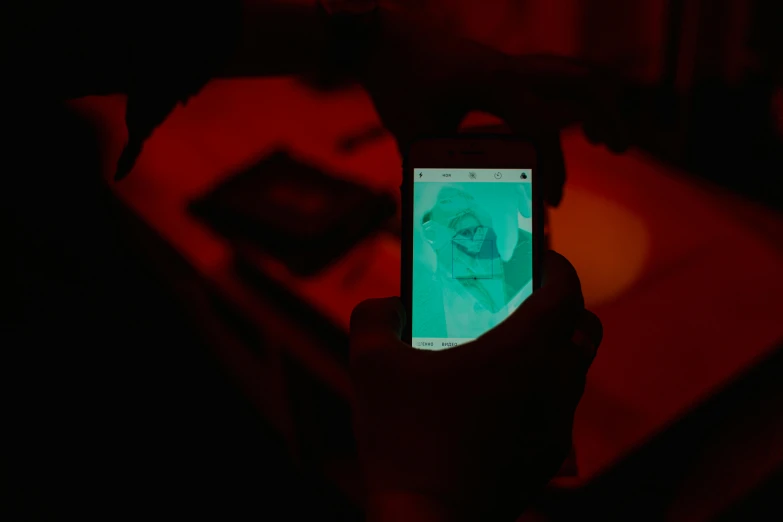 a person holding up a cell phone in a dark room, inspired by Johann Kaspar Füssli, interactive art, red hue, close-up photograph, rectangle, coloured