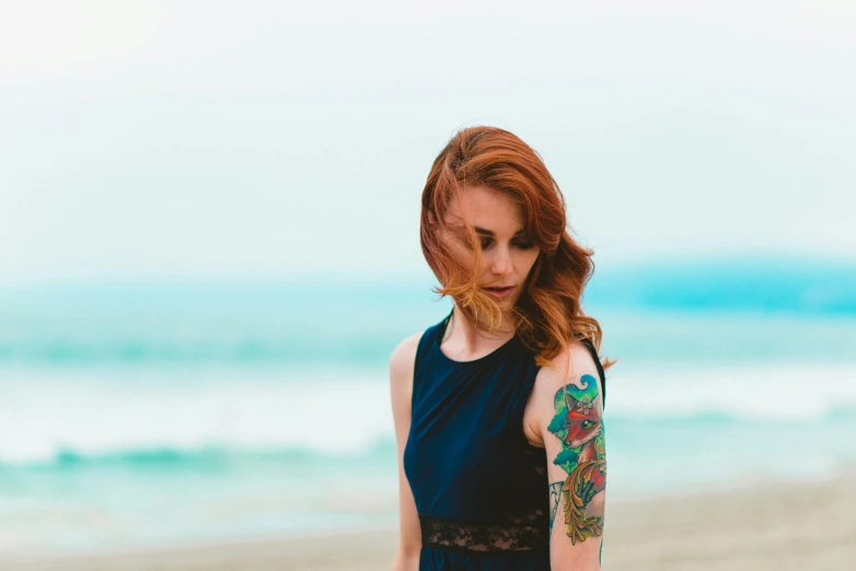 a woman standing on top of a sandy beach, a tattoo, pexels contest winner, realism, cute young redhead girl, tattoo parlor photo, green and blue tones, photograph of a sleeve tattoo