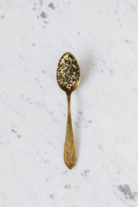 a close up of a spoon on a table, herb, gold speckles, detailed product image, full body in shot