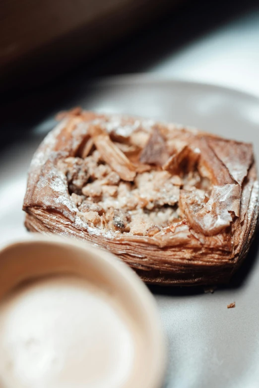 a pastry sitting on top of a plate next to a cup of coffee, by Mathias Kollros, unsplash, square, rotting clay skin, smoked layered, intricate wrinkles