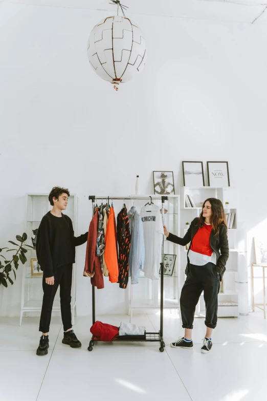 a couple of people standing in front of a rack of clothes, in a room