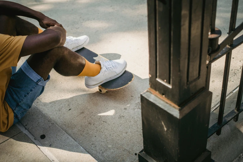 a man sitting on the ground with a skateboard, trending on unsplash, gray shorts and black socks, on a pedestal, ignant, wesley kimler