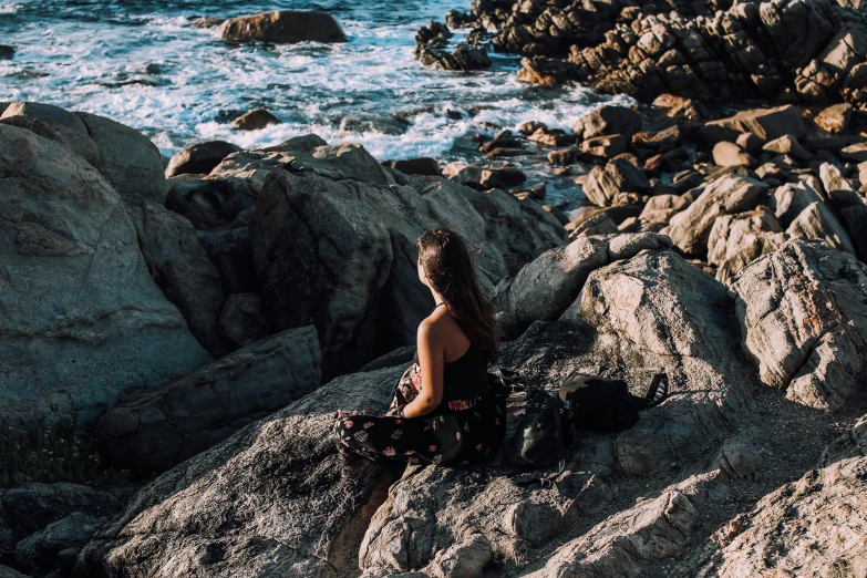 a woman sitting on top of a rock next to the ocean, pexels contest winner, alana fletcher, al fresco, profile image, icon