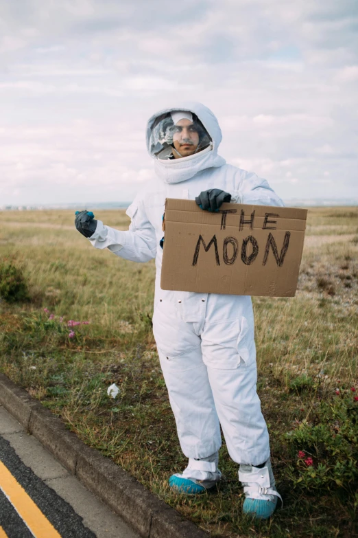 a man in a space suit holding a sign, an album cover, unsplash, street moon landscape, 2019 trending photo, dressed as a scavenger, coast