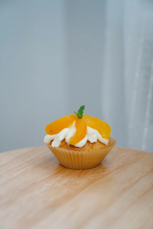 a cupcake sitting on top of a wooden table, orange and white, profile image, mango, full product shot