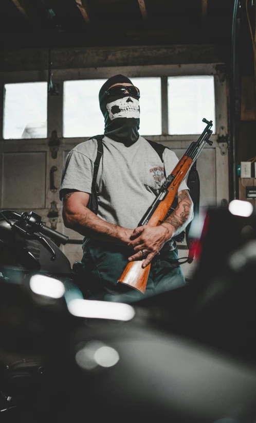 a man in a mask holding a rifle in a garage, a portrait, by Brian 'Chippy' Dugan, pexels contest winner, auto-destructive art, restomod, discord profile picture, bandoliers, anonymous as a car