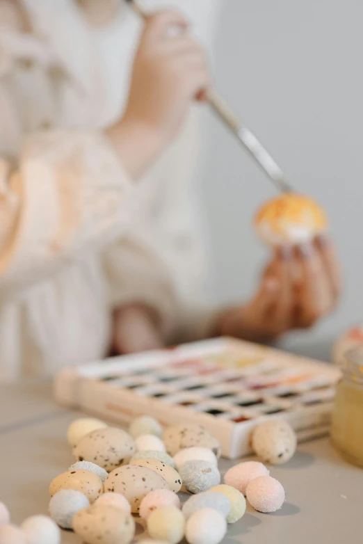 a little girl is painting eggs on a table, pexels contest winner, soft muted colors, promo image, midsommar color theme, professional image