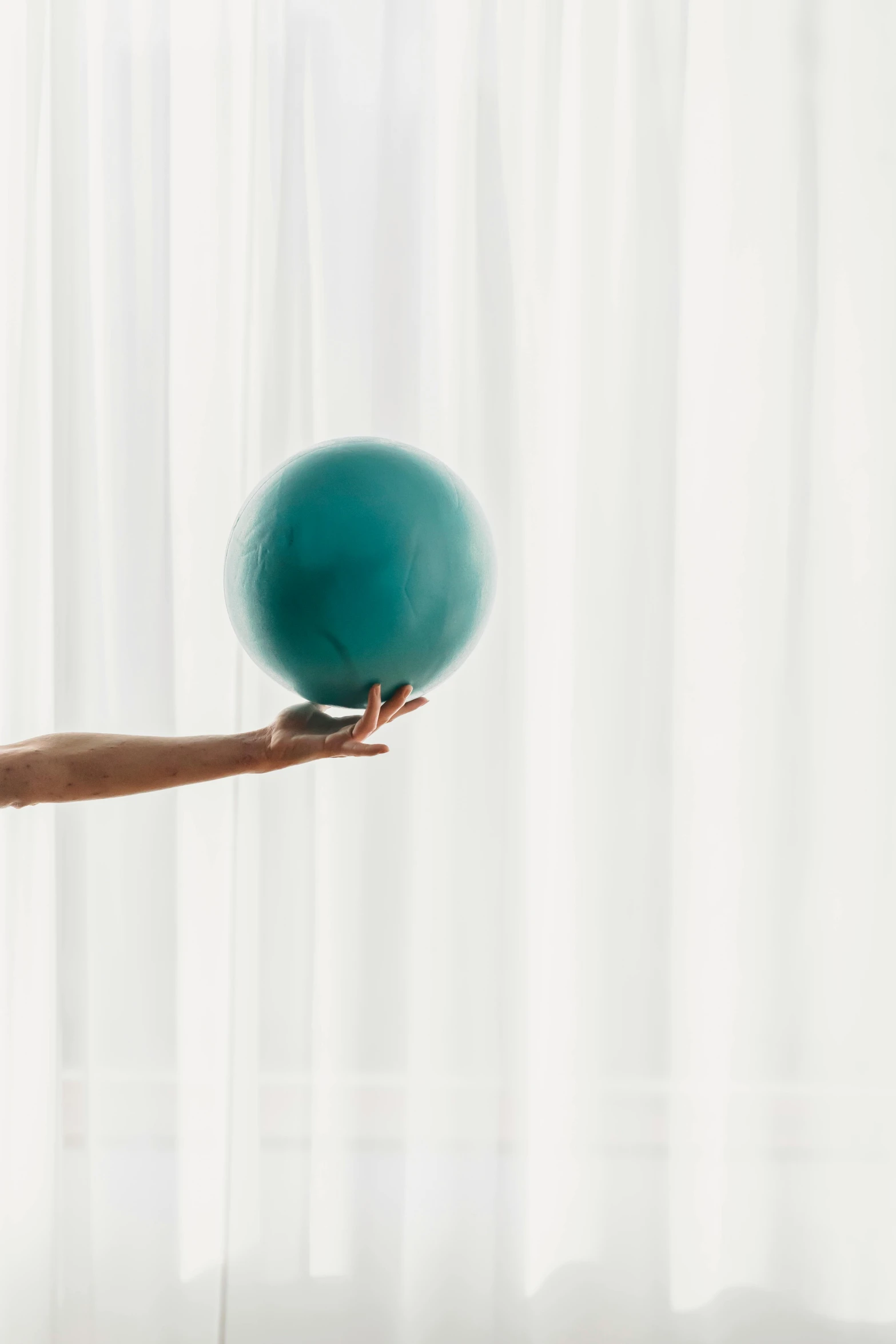 a woman playing with a ball in front of a window, by Arabella Rankin, trending on unsplash, teal electricity, close-up of thin soft hand, set against a white background, round format