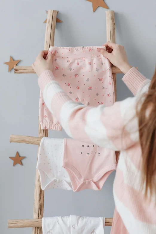 a woman hanging a blanket on a ladder, by Julia Pishtar, trending on pexels, pink and pink details, overflowing with diapers, wearing a cute top, with stars