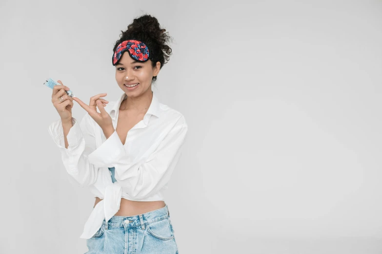 a woman in a white shirt and blue jeans holding a cell phone, trending on pexels, antipodeans, wearing a baggy pajamas, photoshoot for skincare brand, holding a syringe, mixed-race woman
