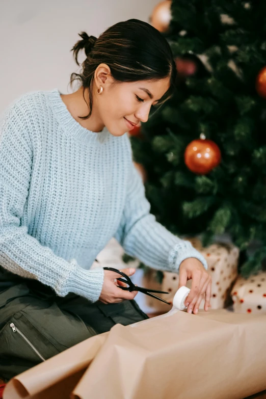 a woman wrapping presents in front of a christmas tree, by Julia Pishtar, wearing casual sweater, thumbnail, manuka, abcdefghijklmnopqrstuvwxyz
