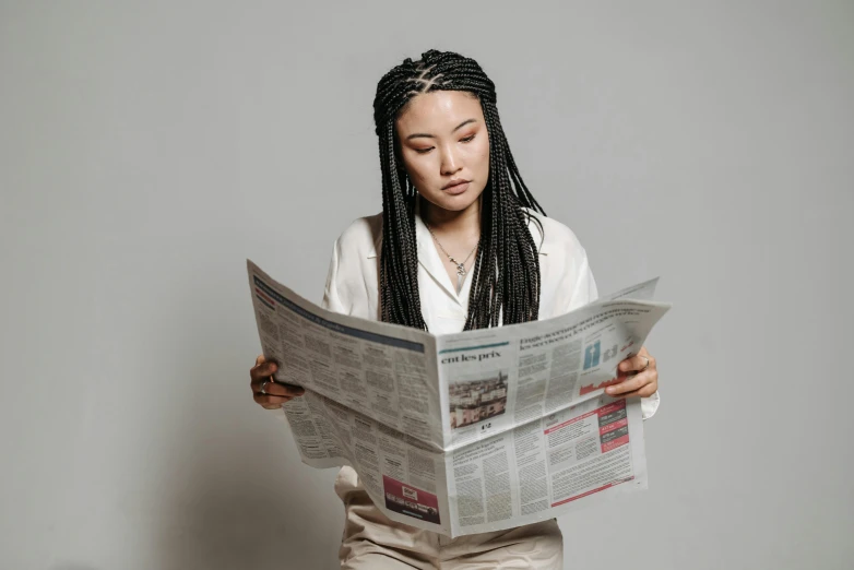 a woman sitting on a stool reading a newspaper, trending on pexels, private press, girl with plaits, ethnicity : japanese, on a gray background, mixed-race woman